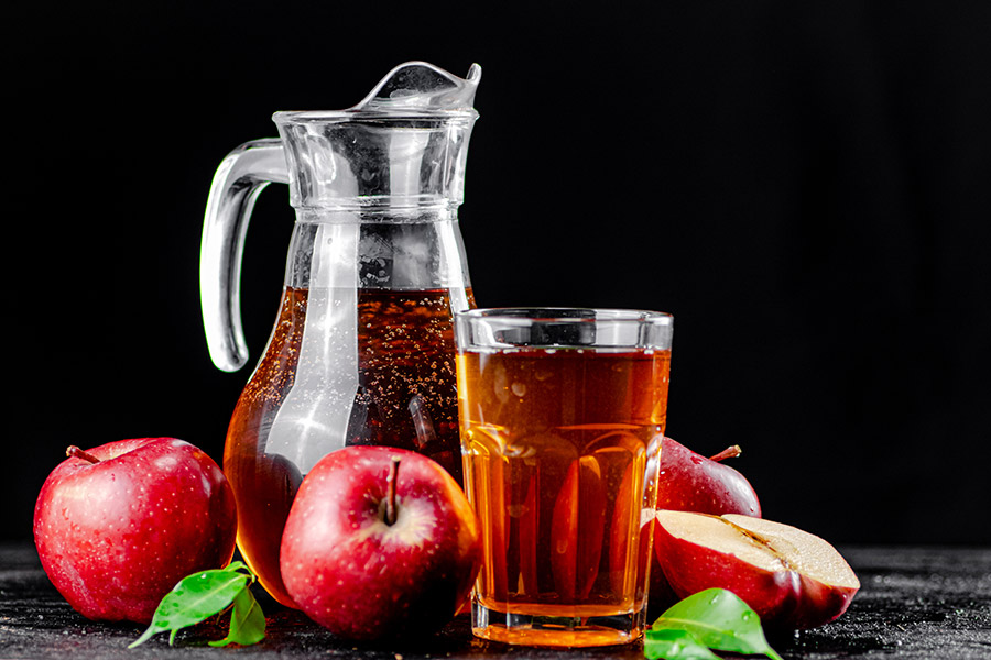 Karaffe und Glas mit Apfelsaft, umgeben von frischen roten Äpfeln.