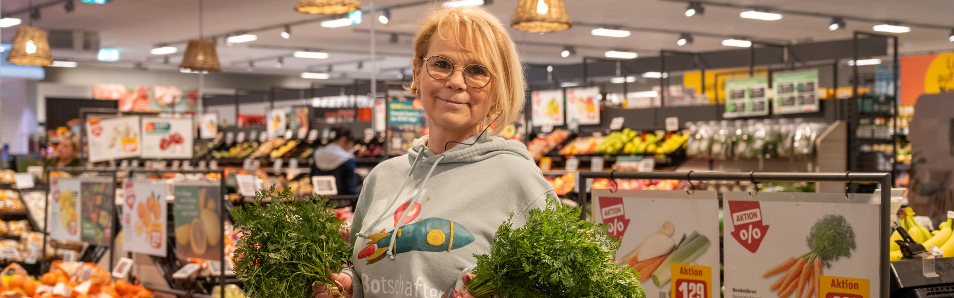 nette Mitarbeiterin lächelt in die Kamera und hält frische Karotten in der Hand